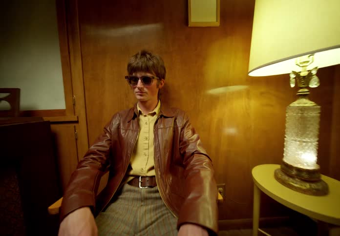 A man wearing a brown leather jacket sits in a room