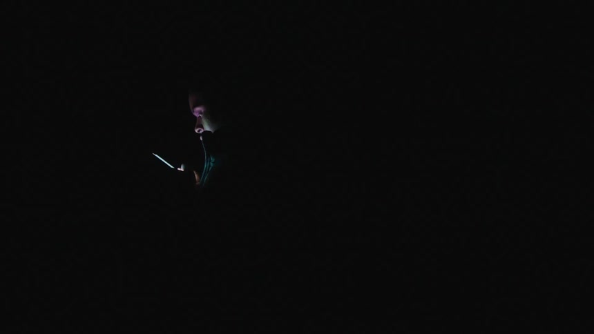 A woman and their man using their smart phones in complete darkness except for the light from their phones