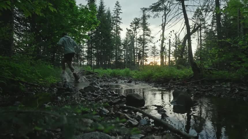 A man running through the woods jumps over a small pond