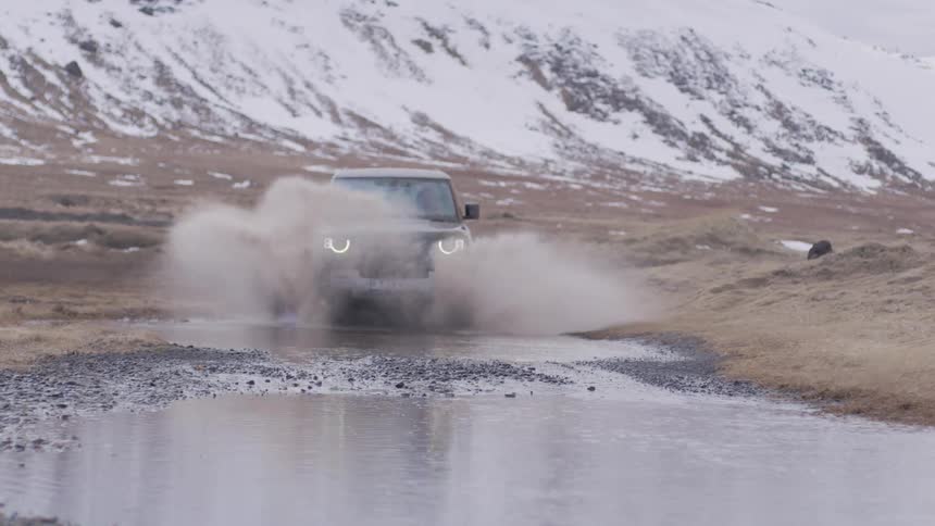 Truck passing through a puddle in a natural environment with snowcovered mountains nearby