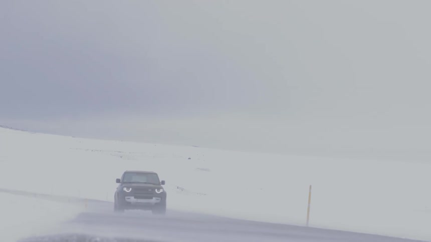 A car driving along the road in a frozen mountainous landscape during a blizzard