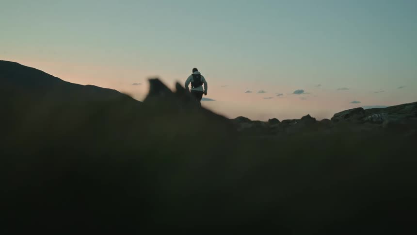 A person with a small backpack is running on a ground with grass and stones