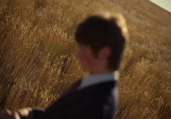 Man in a suit in the middle of the woods cleaning his sunglasses