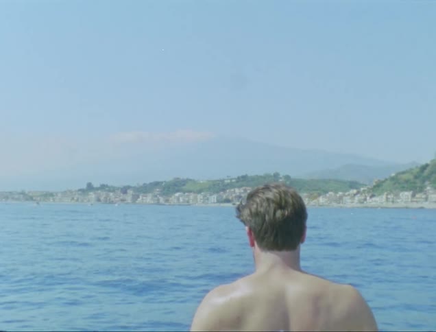 Shirtless man back turned taking photos of the sea