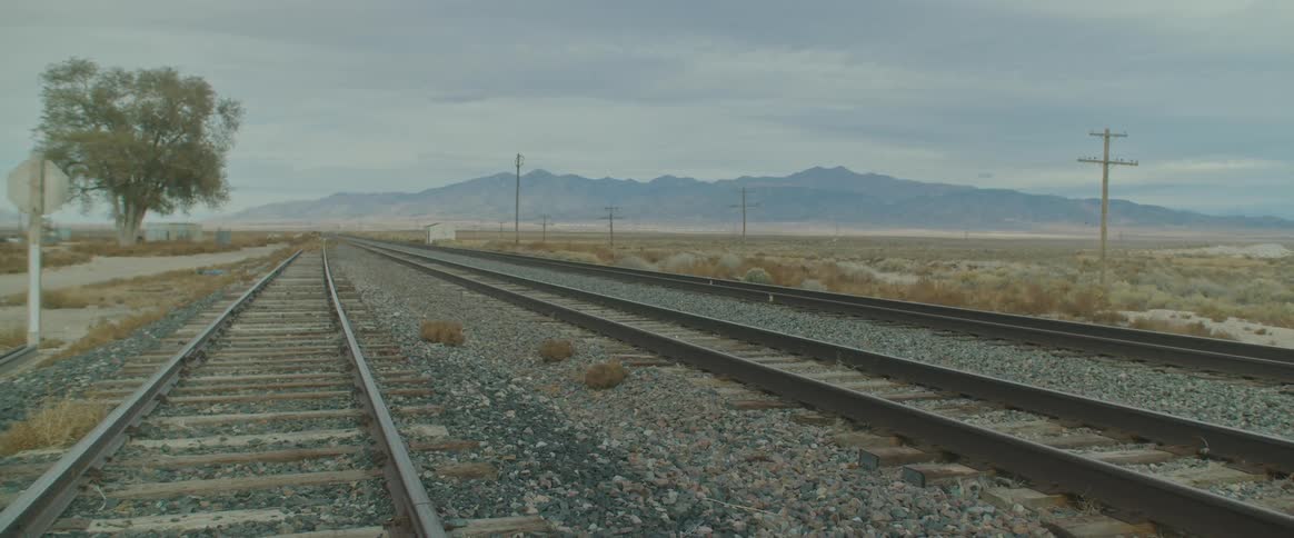 Railway tracks stretch across the land with mountains in the distance under a cloudy sky