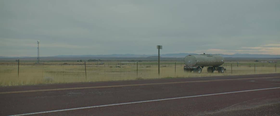 A truck load is parked in a field of dry grass next to a road