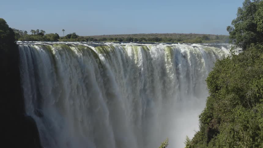 Wide waterfall flows down cliff across from tree covered steep slopes