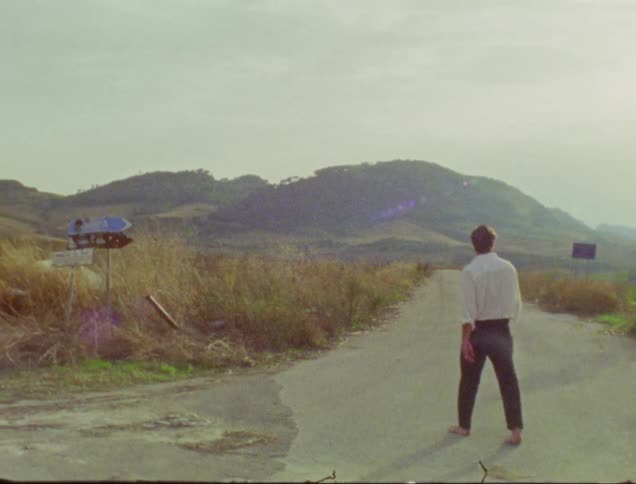 Barefoot man in formal attire walking on a street in the midst of nature