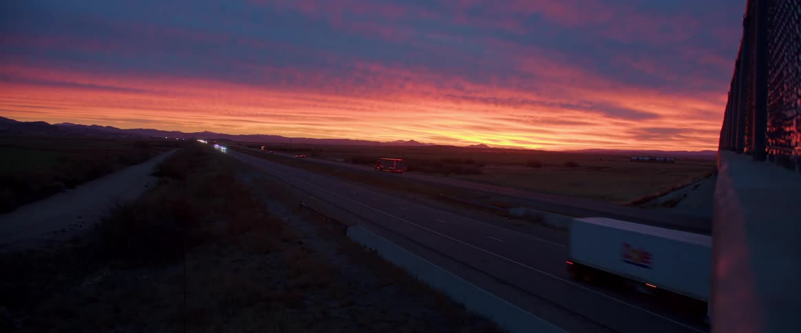 Semi trucks drive along highway under a bright red sky