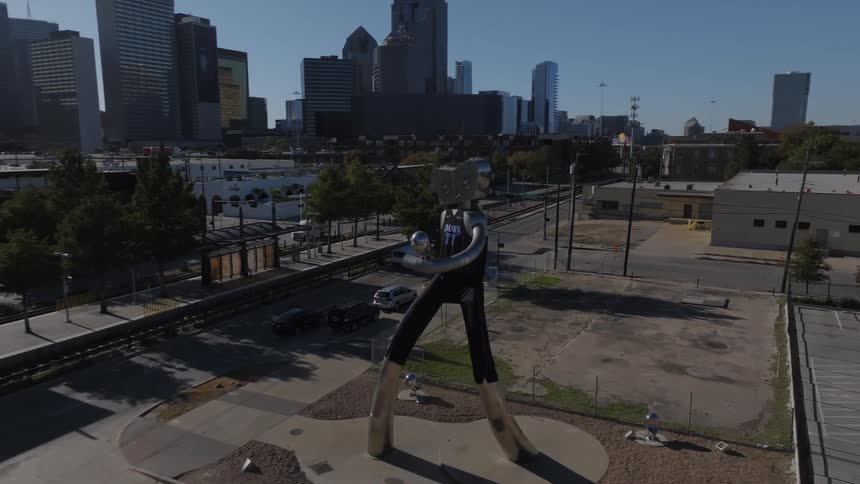 Robot traveling man sculpture with downtown dallas and blue sky in the background on a sunny day
