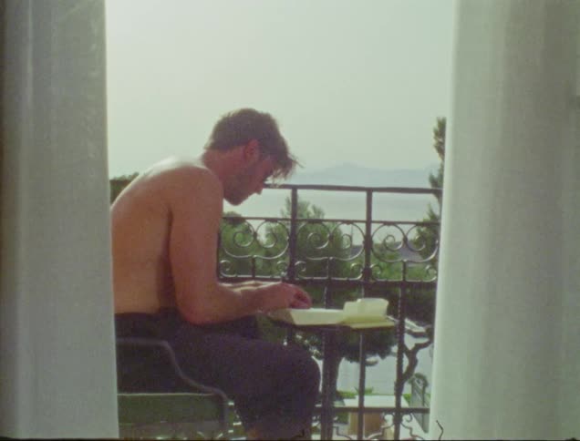 A man writing sitting on the balcony of a building