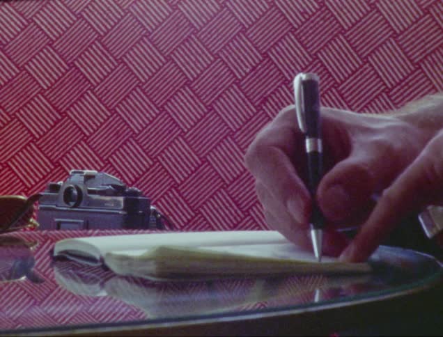 A photographer writes in a notebook while seated at a round glass table