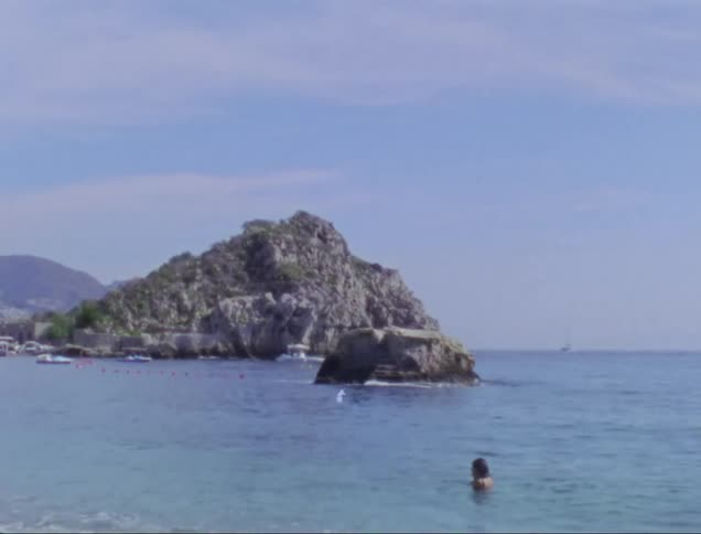 Woman swimming on a beach next to a rock promontory