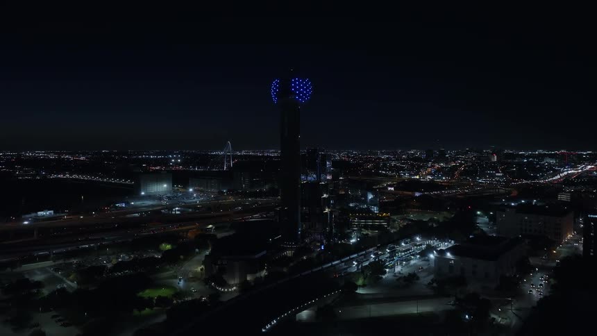 Colorful light display covers top of tower standing between a busy highway and the waterfront at night
