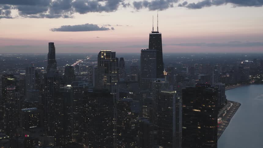 Yellow window lights dot a darkening city skyline against a purple sky