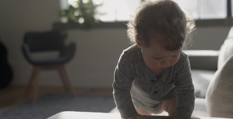 A baby is crawling over the side of a couch