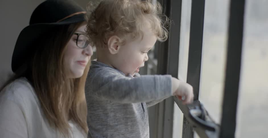 A woman watches a baby play by a window