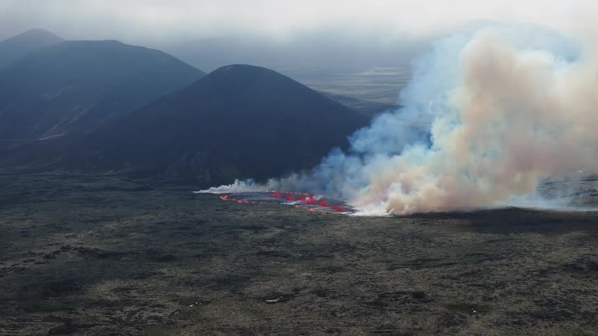A region close to the mountain is burning and releasing a lot of white smoke into the sky