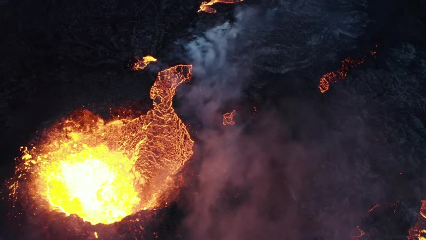 Molten hot lava glows in the darkness as it splashes and flows from an erupting volcano