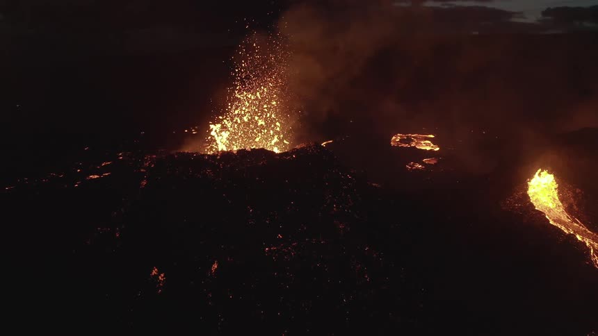 A volcano explodes with lava at night