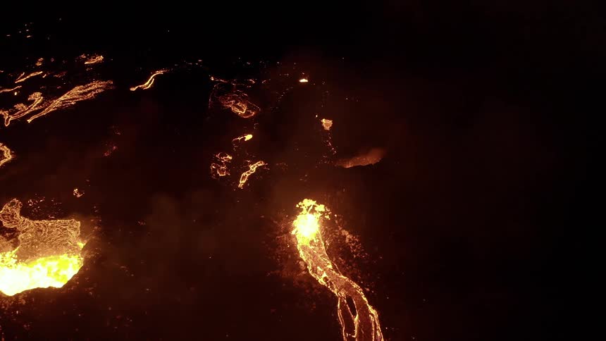 Molten hot lava glows in the darkness as it splashes and flows from an erupting volcano