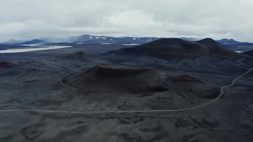A single vehicle drives along a road that passes through a hilly landscape
