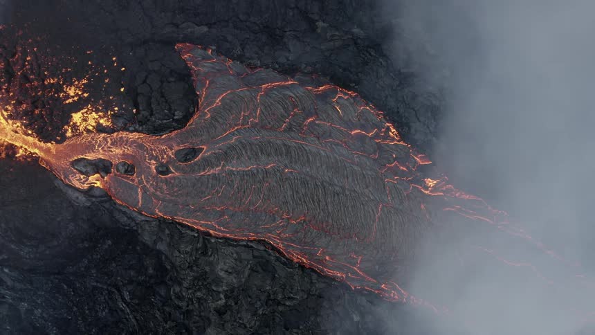 Molten hot lava glows as it splashes from an erupting volcano as smoke rises and lava flows