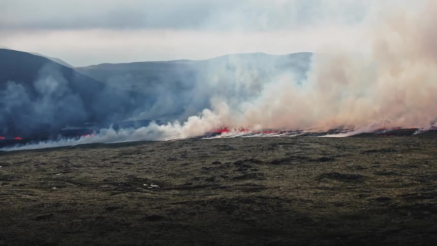 Smoke rises as glowing hot lava flows and splashes across the land