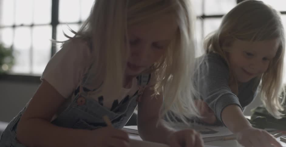 Two girls color with sun streaming in windows in the background