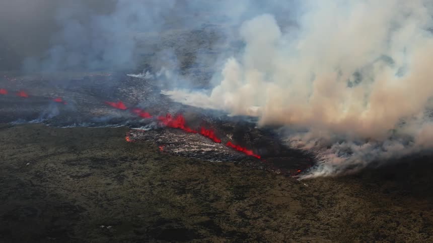 Smoke rises as glowing hot lava from an erupting volcano splashes and flows across the land