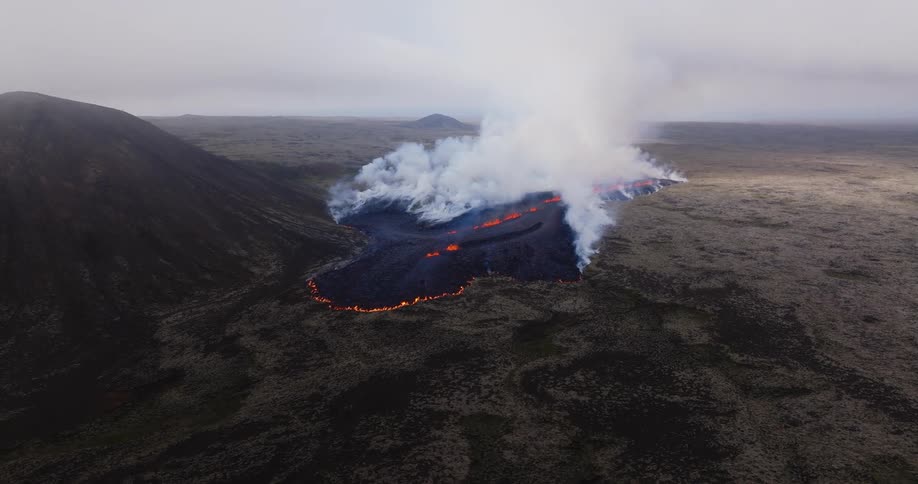 Smoke rises as flaming hot lava from an erupting volcano flows across the land