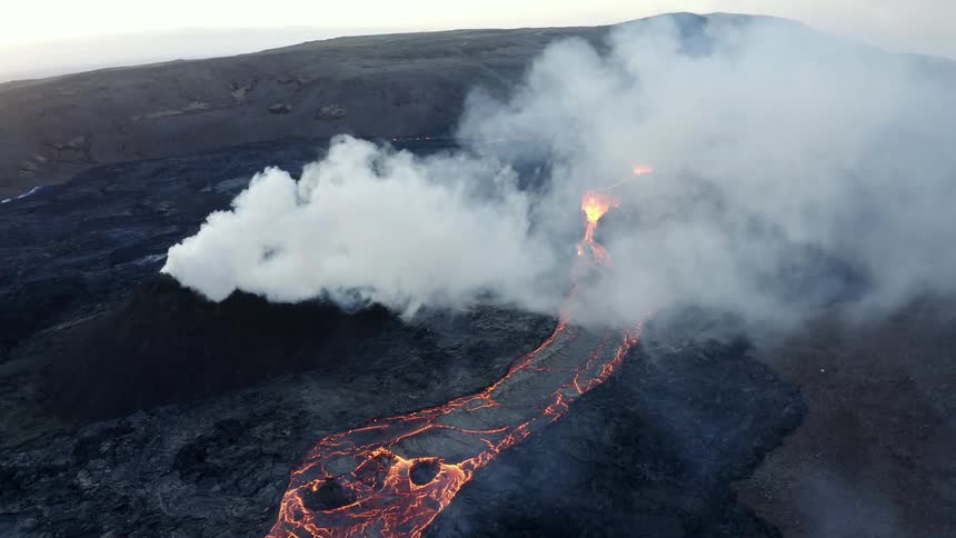 Smoke rises as flaming hot lava from an erupting volcano flows across the land