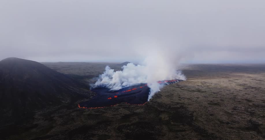 Aerial landscape of a volcano erupting outdoors next to a mountain during day time