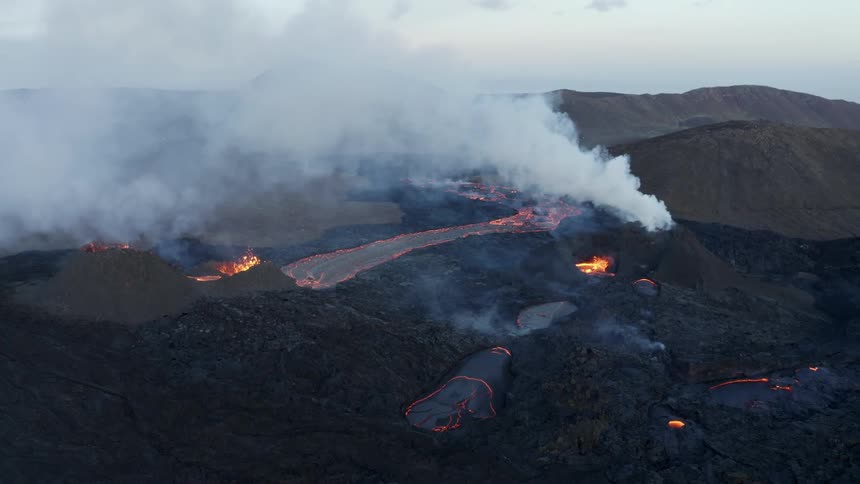 Smoke rises as glowing hot lava from an erupting volcano splashes and flows across the land