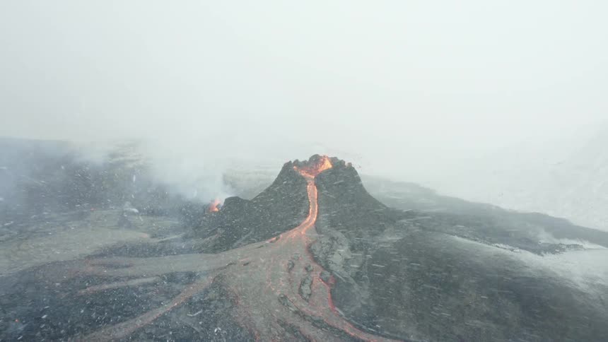 Volcano erupting with lava flowing while its snowing
