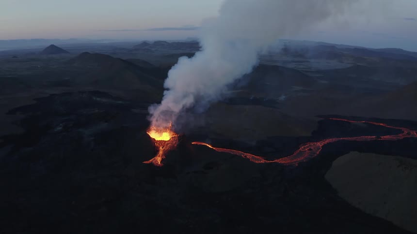 Molten hot lava glows as it splashes from an erupting volcano and smoke rises as lava flows