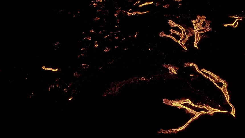 Molten hot lava glows in the darkness as it flows from an erupting volcano