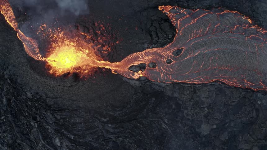 Molten hot lava glows as it splashes from an erupting volcano and flows across the land