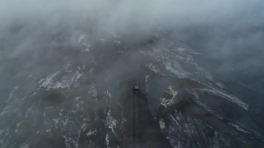 Vehicle drives along road through frozen terrain under low lying clouds