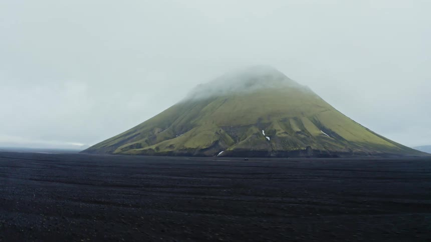 Landscape of a green mountain next to a vast area of dark flat lands