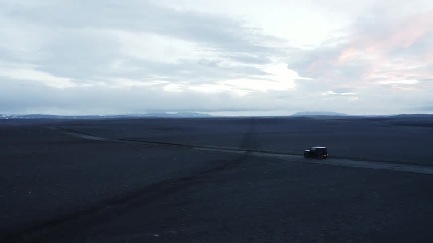 Vehicle drives on road through barren landscape on cloudy day