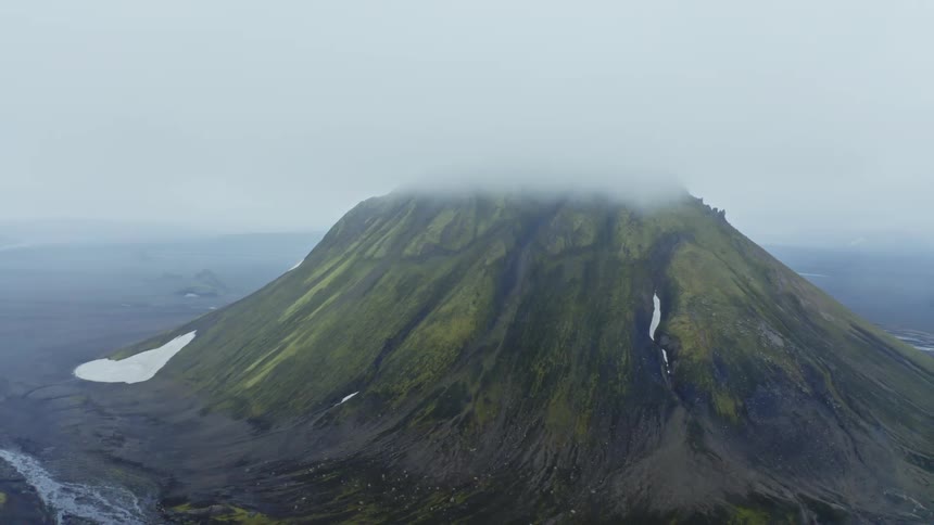 River flows across plain past mountain with a few patches of snow on a foggy day
