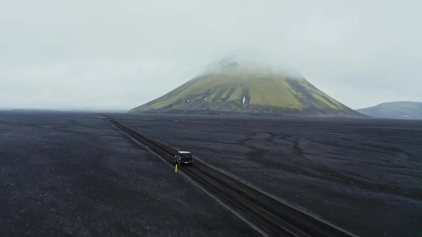 Aerial view of black jeep driving down a road in the desert with a high mountain in the background