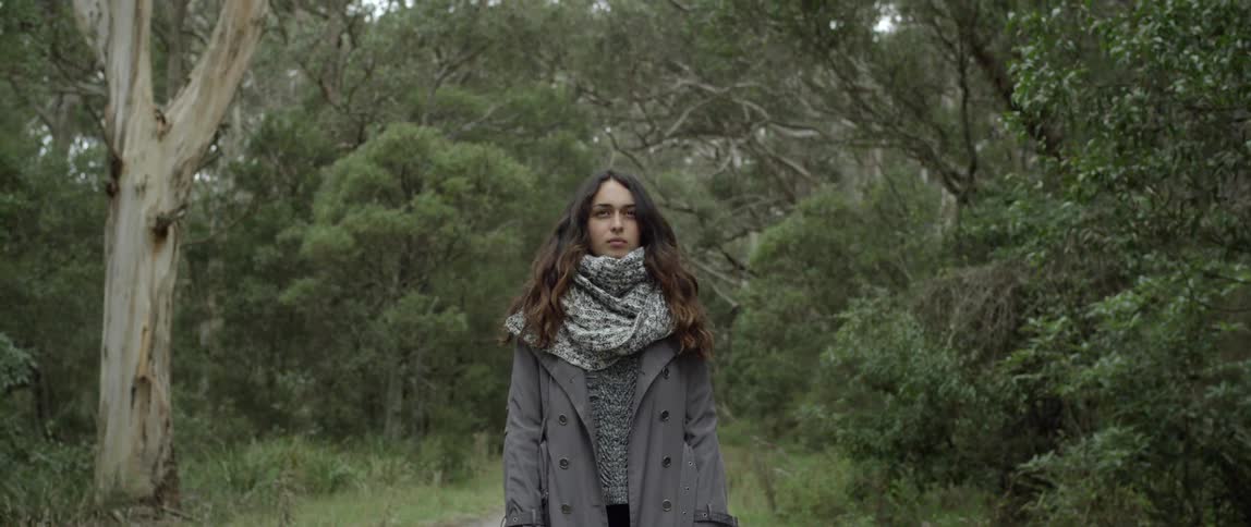 A woman is standing with a forest behind her