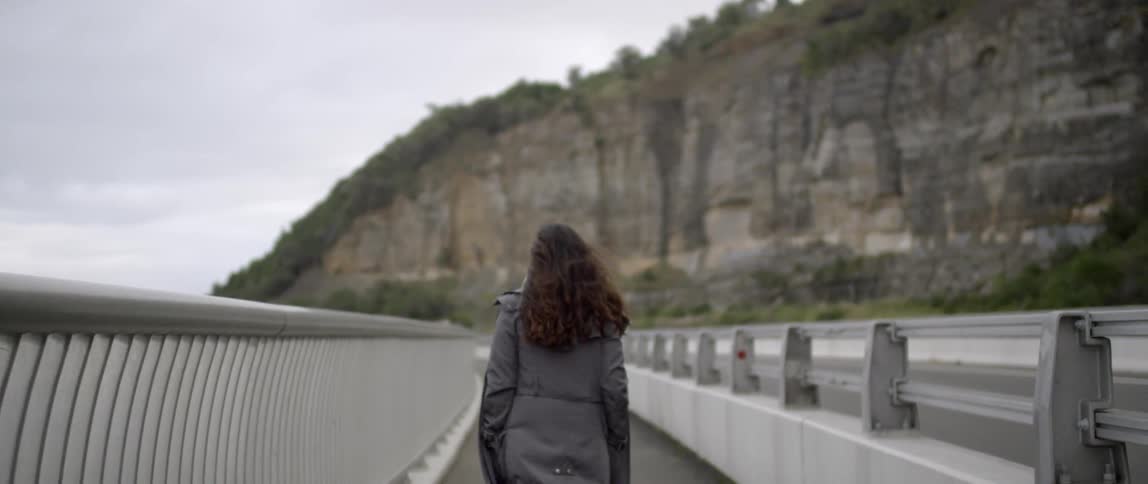 A woman is walking along a railing towards a mountain