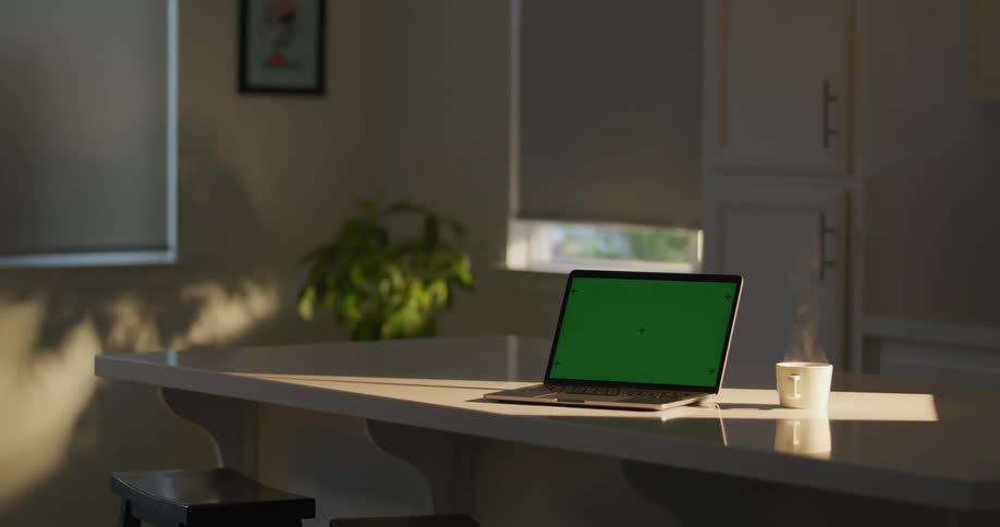 A laptop computer with a green screen on a table as steam rises from a cup of coffee