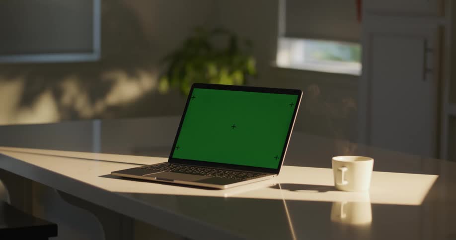 A laptop computer and a steaming coffee mug sit on an office desk