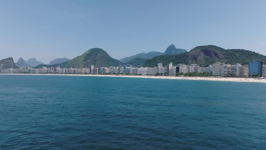 Aerial view of buildings along beach coastline during the day mountains on horizon
