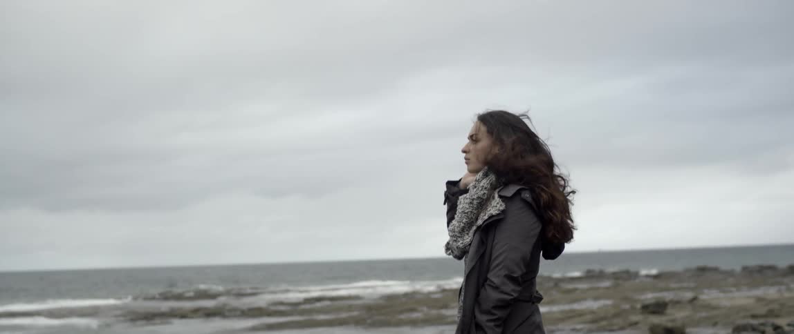 A woman brushes her hair on the windy shore