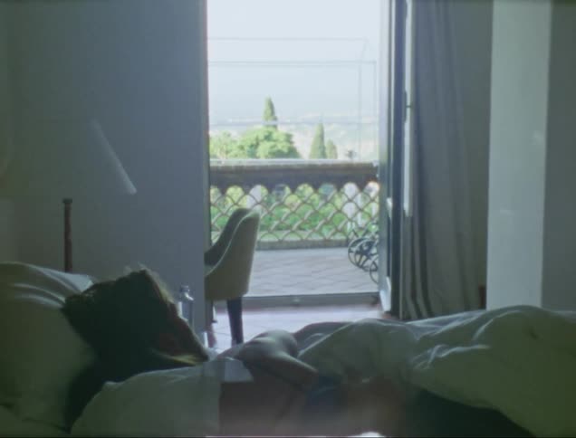 Man lying in bed caresses womans shoulder and looking out the balcony door in the morning